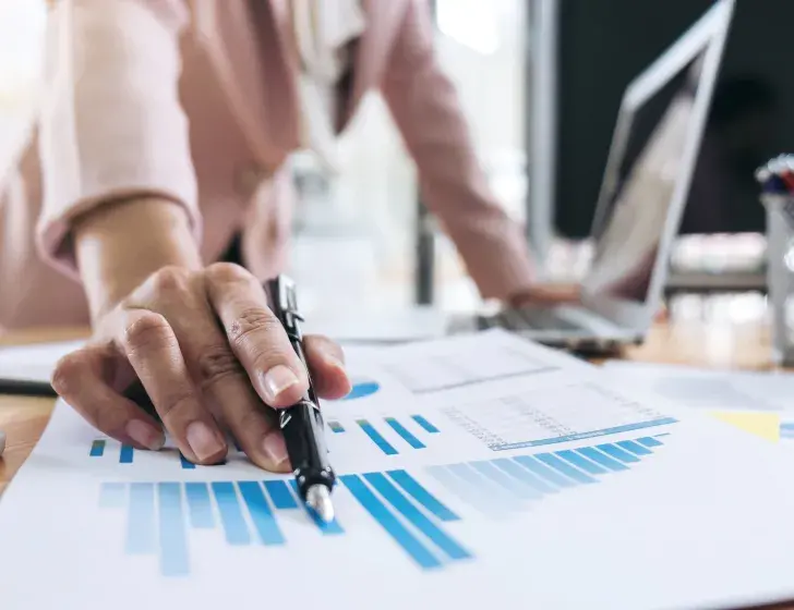 Woman's hand with pen pointing at data visualizations.